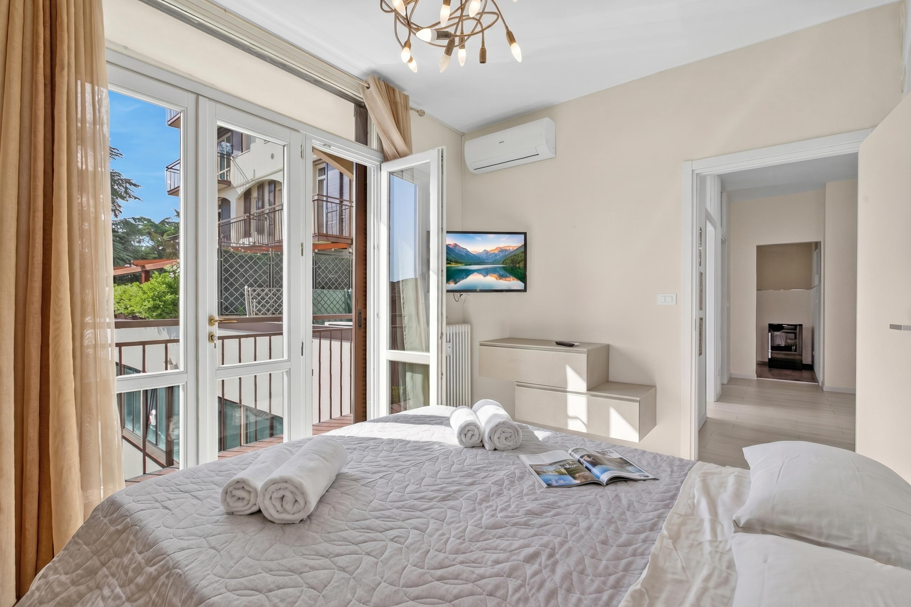 Una camera d'albergo con un letto, una scrivania, una sedia, una finestra con tende e vista su un balcone.
