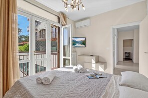A hotel room with a bed, a desk, a chair, a window with curtains, and a view of a balcony. - Bono Deluxe: 3BR Home in Desenzano (Desenzano del Garda)