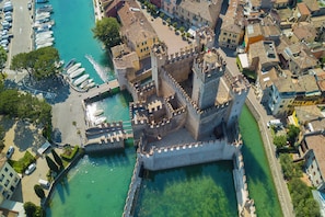An aerial view of a historic fortified castle with a moat, surrounded by residential buildings and a marina with boats.