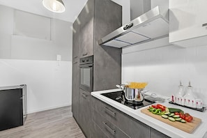 A modern kitchen with a built-in oven, a stovetop, and a wooden cutting board with vegetables.