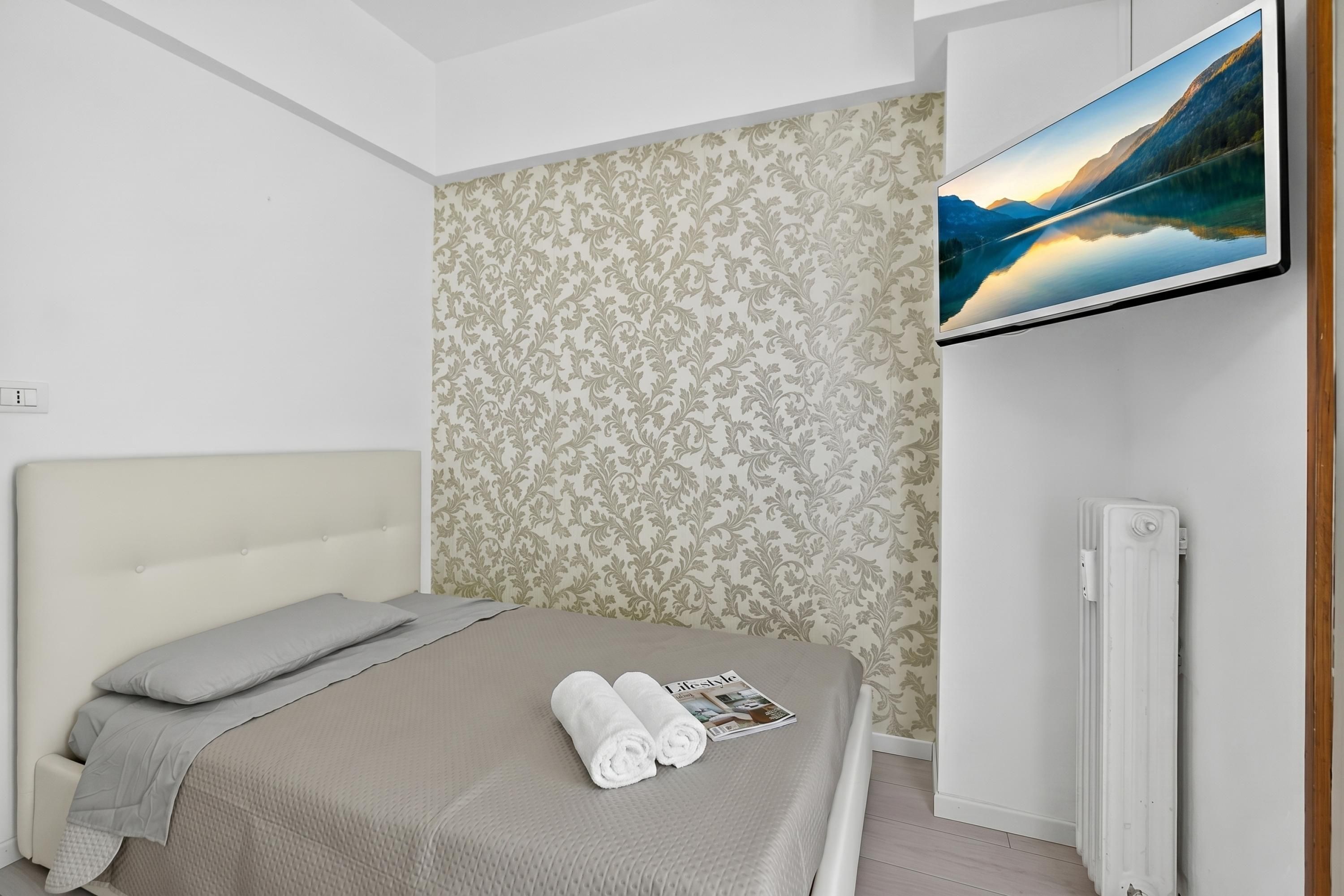 Une chambre à coucher avec un lit, un téléviseur fixé au mur et un radiateur.