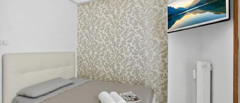 A bedroom with a bed, a wall-mounted TV, and a radiator.