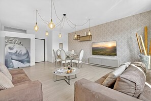 A modern living room with a dining area, a sofa, a coffee table, and a TV mounted on the wall. - Bono Deluxe: 3BR Home in Desenzano (Desenzano del Garda)