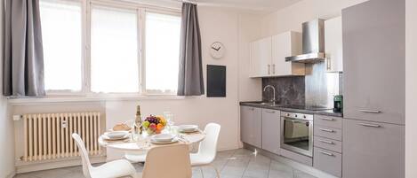 A modern kitchen with a dining area, including a table set with plates, glasses, and a fruit bowl.