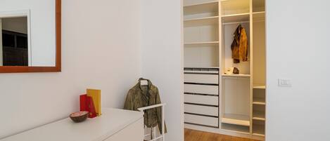 A modern room with a white dresser, a mirror, a coat rack, and a walk-in closet with shelves.