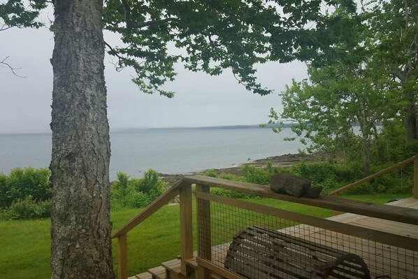 A wooden deck with a railing overlooking a body of water, surrounded by greenery.