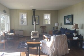 A cozy living room with a wood-burning stove, a sofa, a chair, a table, and a lamp.