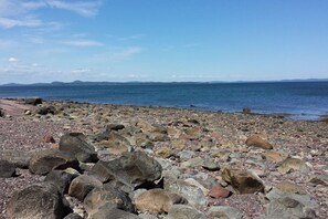 A rocky beach with large boulders and a clear view of the sea and distant mountains.