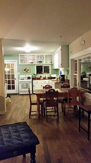 A compact kitchen with white cabinets, a stove, and a dining area with wooden chairs and a table.