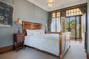 A bedroom with a large bed, two bedside tables, a nightstand, a chandelier, and a view of the outdoors through a glass door. - Earnscleugh Castle (Alexandra)