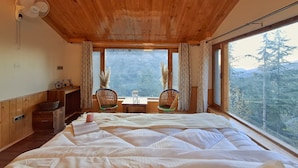 Una camera in legno con un letto, un tavolo con sedie, una finestra con tende e vista sugli alberi.