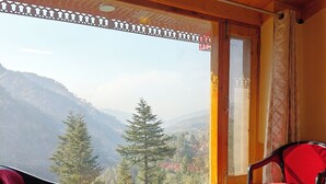 Una stanza con soffitto in legno, una finestra vista montagne, due sedie con cuscini rossi e un tavolo in legno.
