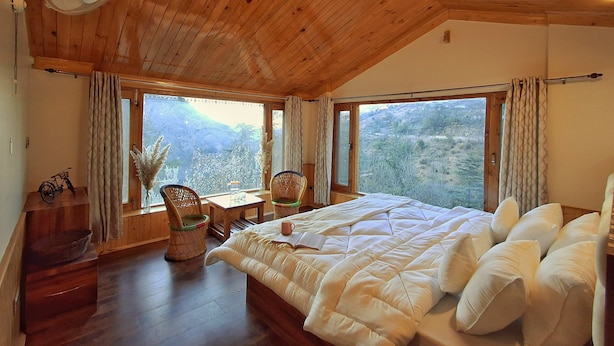 Una camera da letto con soffitto in legno, un letto, un tavolo, sedie e vista sull'esterno.