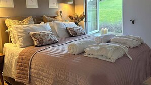 A bedroom with a large bed, a bedside table, a lamp, a window with a view, and framed pictures on the wall. - Rose Cottage, Cosy South Lake District Retreat, Sleeps 5 (Marton)