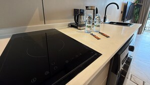 A modern kitchen with a black induction cooktop, a coffee maker, and two water bottles on the counter. - 412 Tara-jre Jabal Al Lweibdeh With Stunning View (Amman)