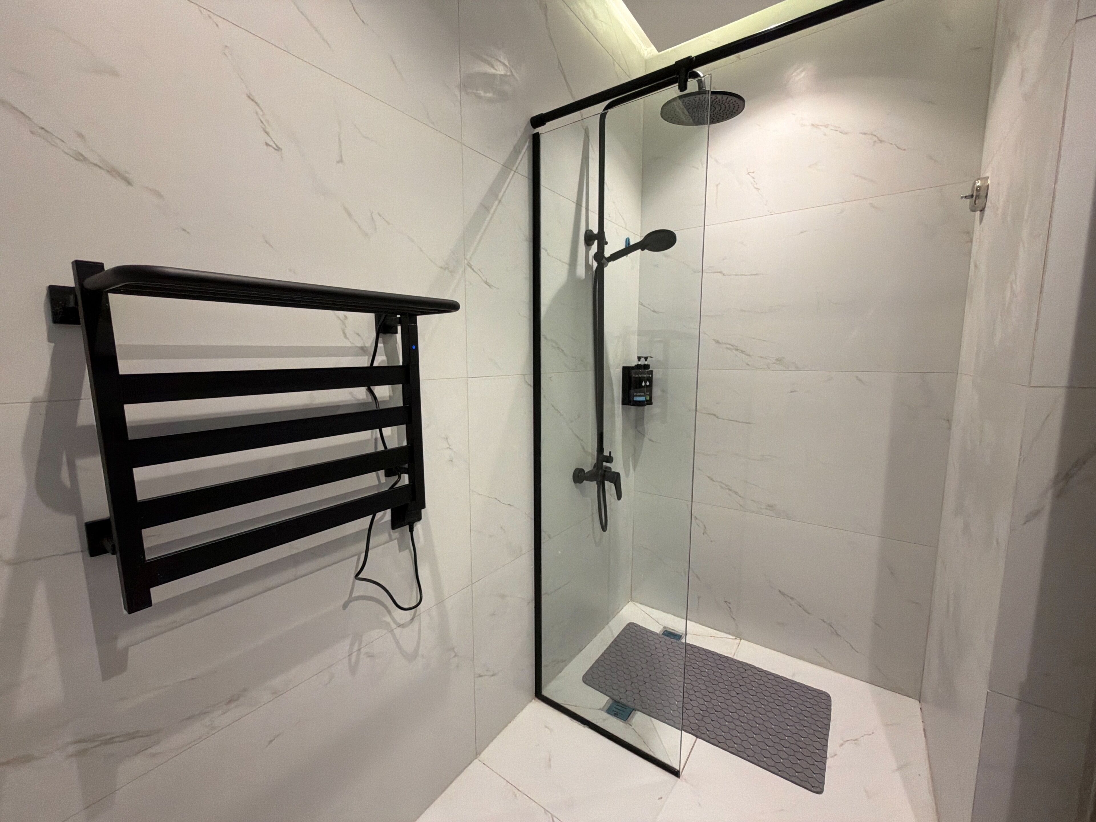 A glass-enclosed shower with a handheld showerhead, a black towel rack, and a small step leading into the shower.