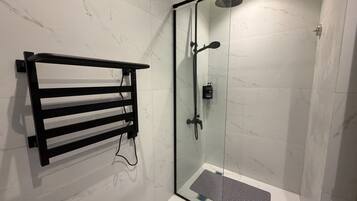 A glass-enclosed shower with a handheld showerhead, a black towel rack, and a small step leading into the shower.