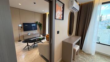 A modern hotel room with a flat-screen TV, a desk, a chair, a small table, and a potted plant.