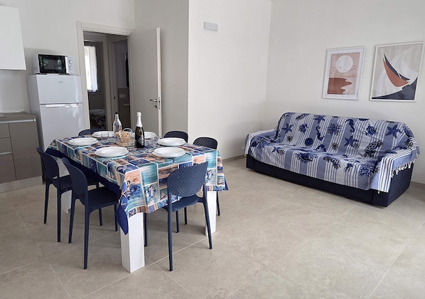 Ein Essbereich mit einem Tisch für vier Personen, einer Couch, einer Mikrowelle und einem Kühlschrank im Hintergrund.