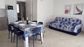 Una zona de menjador amb una taula preparada per a quatre persones, un sofà, un microones i un frigorífic.
