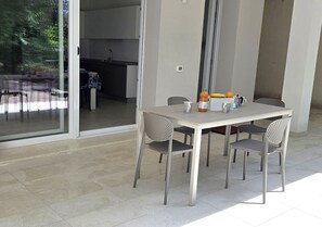 Ein Essbereich mit Tisch und Stühlen, im Hintergrund eine Küche und eine Glastür, die zu einem Außenbereich führt.