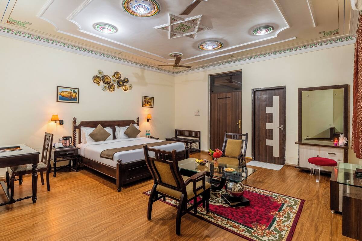 Habitación de hotel con cama, escritorio, sillas, mesa de comedor y ventilador de techo.
