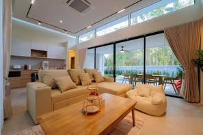 A modern living room with a sofa, coffee table, and dining area. - Radarin Villa (Hat Yai)