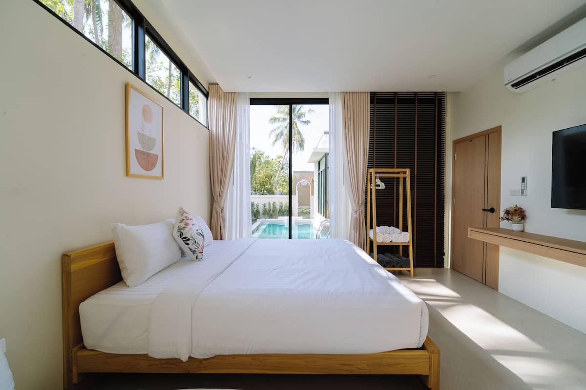 A bedroom with a bed, a TV, a window, and a view of a pool.