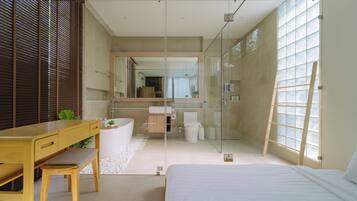 Un baño moderno con cabina de ducha de vidrio, un escritorio de madera y una cama grande.