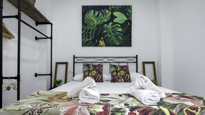 Una cama bien tendida con ropa de cama floral, un cuadro de pared con temática tropical y un cabecero de metal negro.