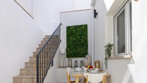 Una escalera lleva a un balcón con una mesa lista para comer, una planta en maceta y una ventana.