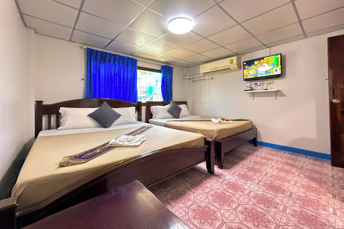 Habitación de hotel con dos camas, televisión, aire acondicionado y ventana con cortinas azules.
