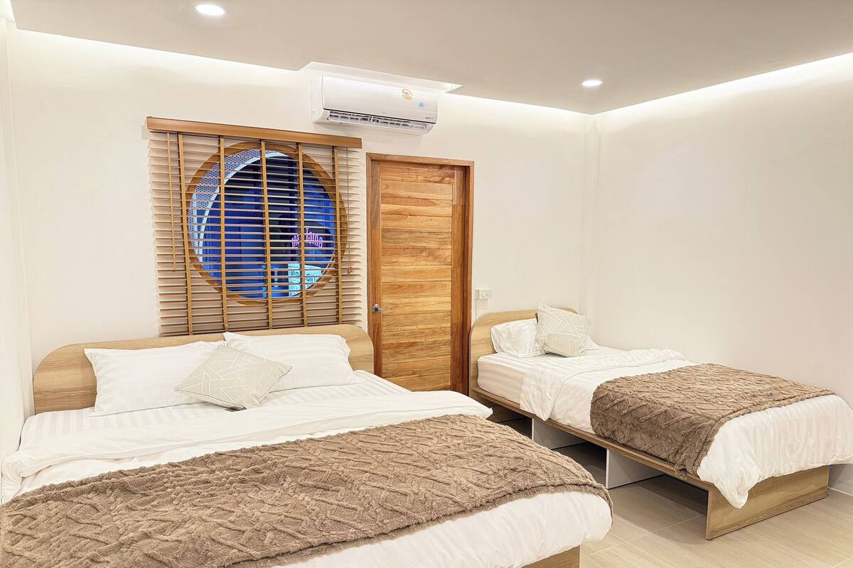 Habitación de hotel con dos camas, un armario de madera, una ventana con persianas y un equipo de aire acondicionado.