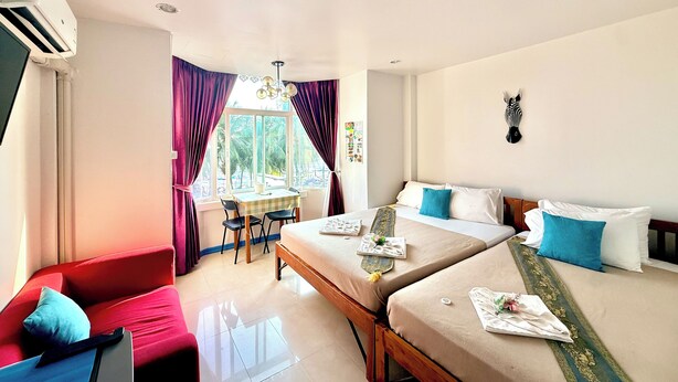 A hotel room with two beds, a dining table, a red sofa, and a zebra head on the wall. - Kelly Hotel Bangsaen (Chonburi)