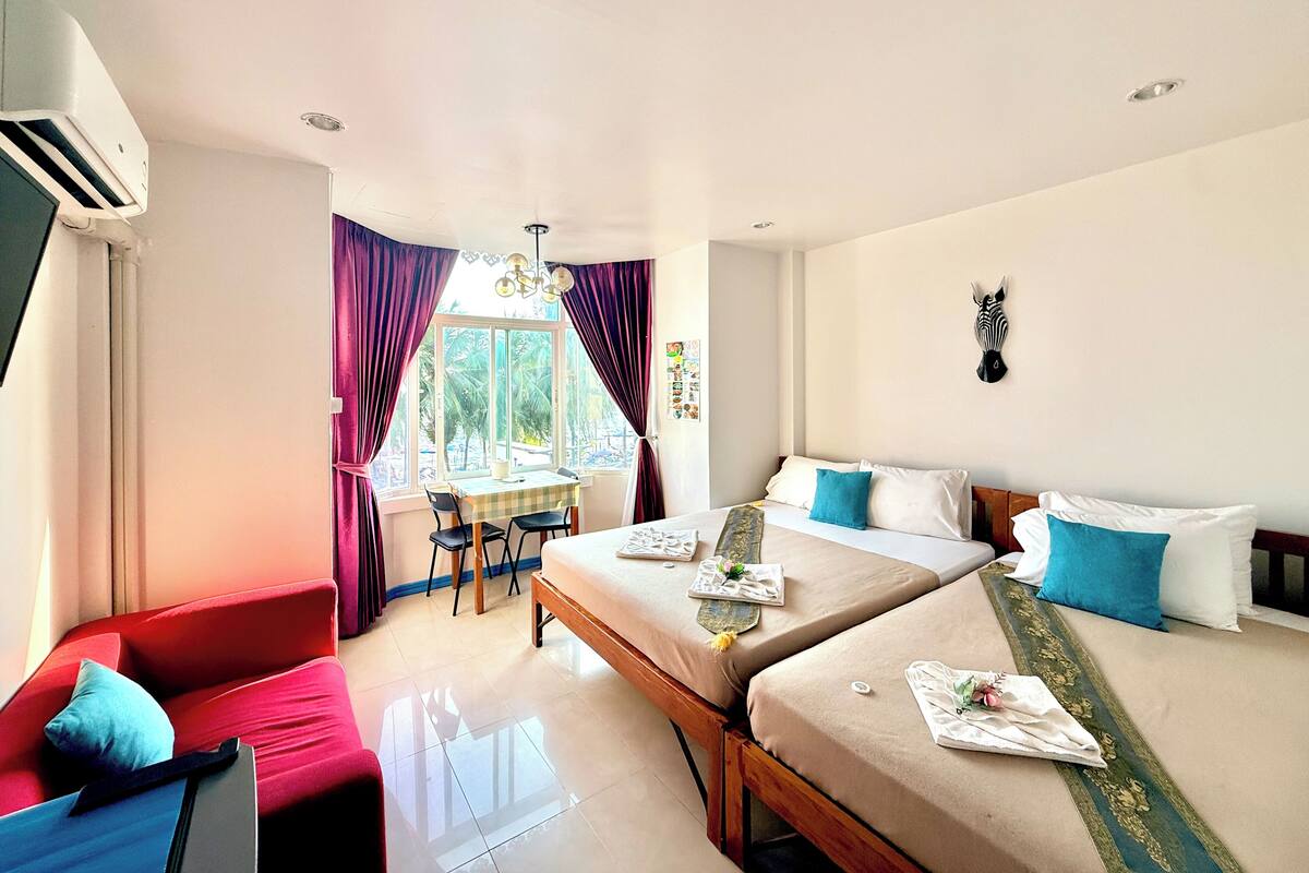 Habitación de hotel con dos camas, una mesa de comedor, un sofá rojo y una cabeza de cebra en la pared.