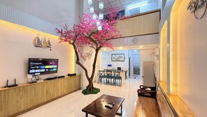 Un hall de hotel con un mostrador de recepción, un banco de madera, una zona de comedor y un árbol decorativo.