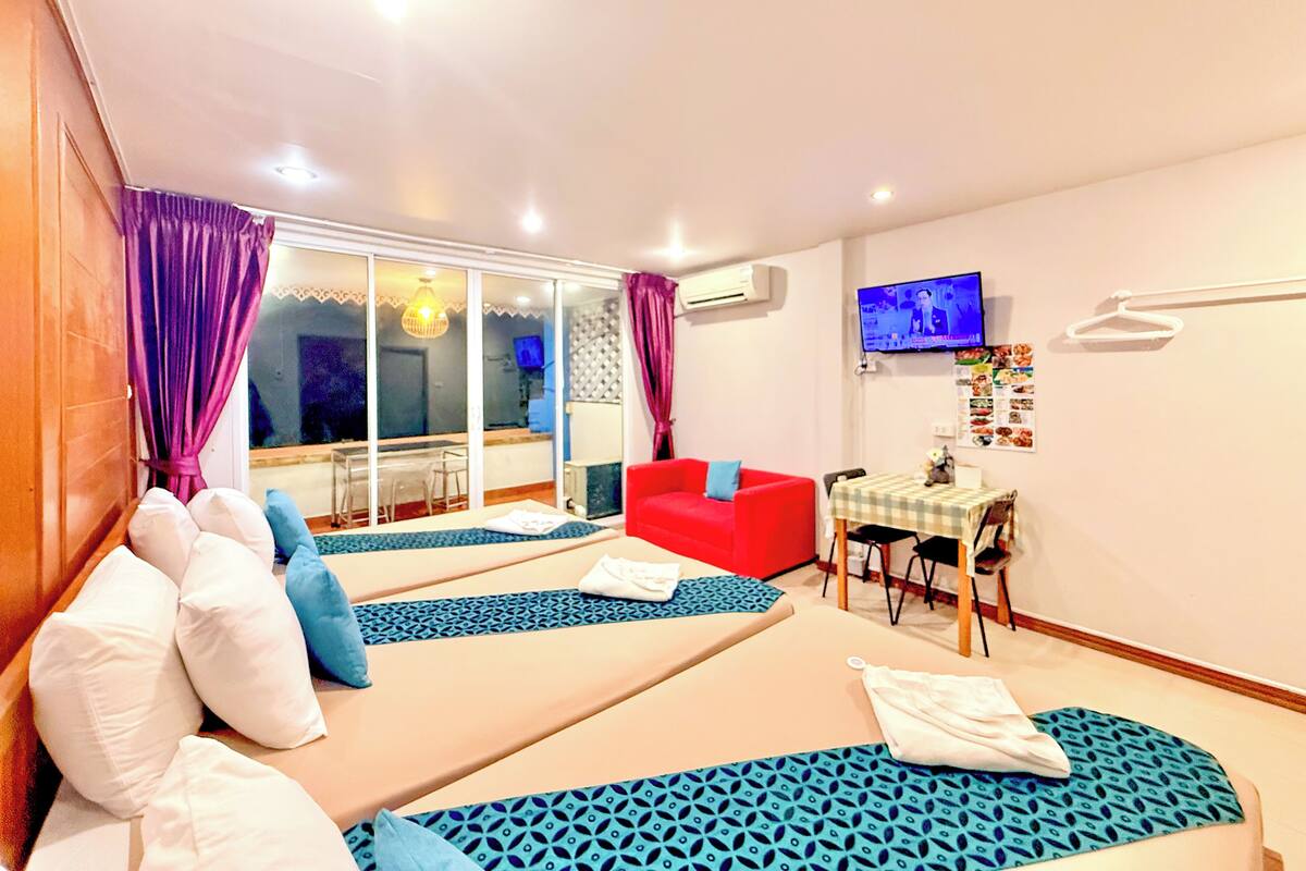 Una habitación con dos camas, un sofá rojo, una mesa de comedor y un televisor en la pared.