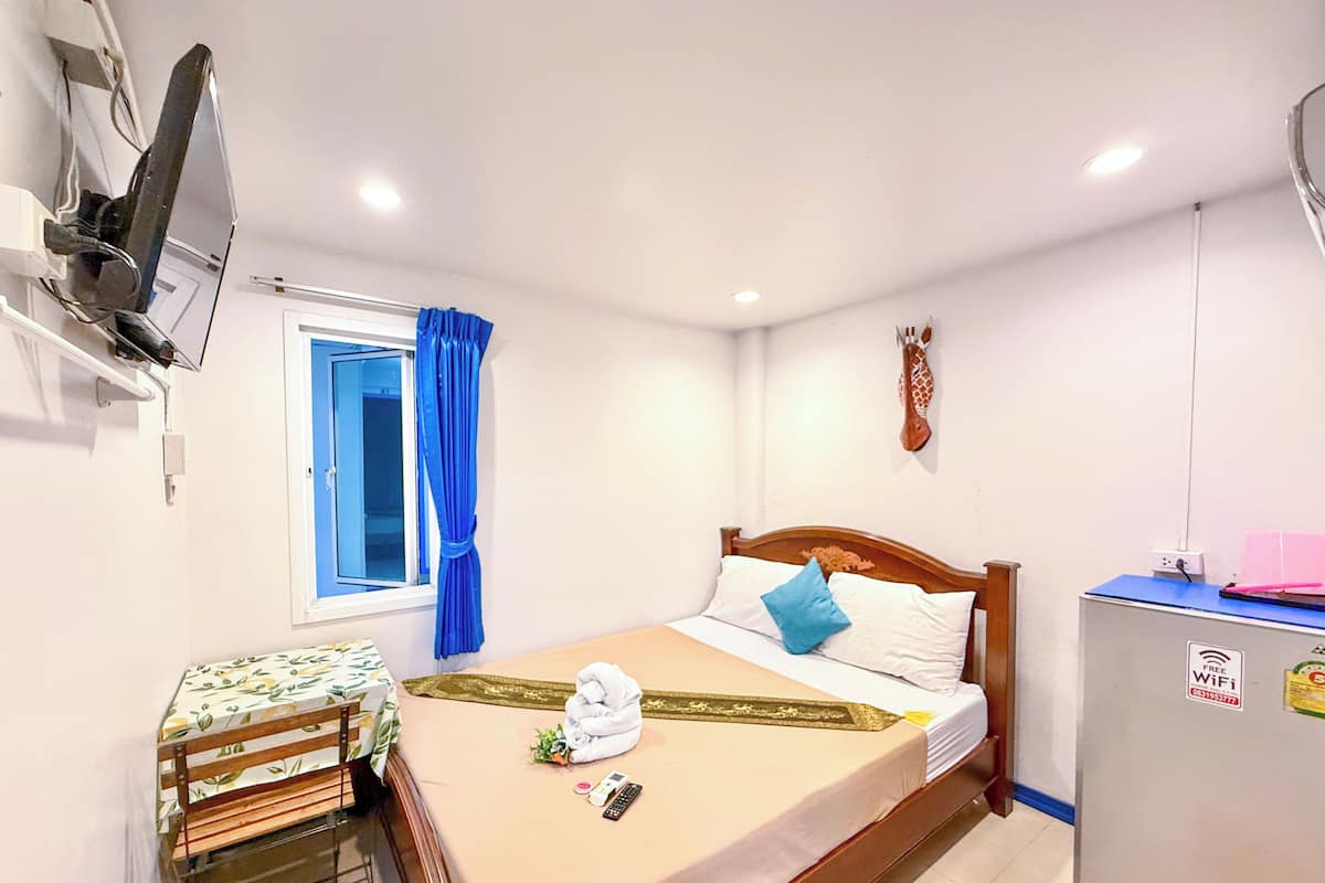 Habitación de hotel con una cama, un escritorio con silla, un televisor fijado a la pared, una ventana con cortinas y un calentador en la pared.