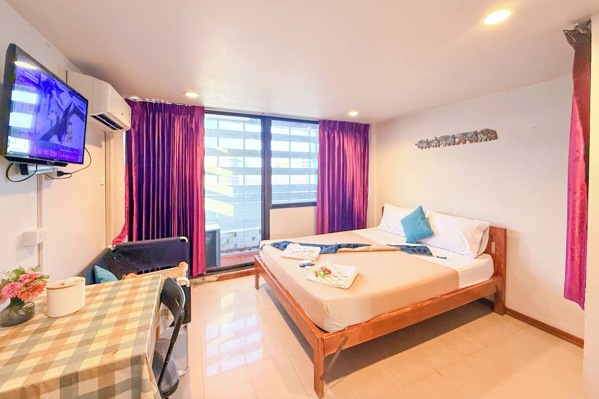Una habitación de hotel con cama, escritorio, silla, televisor y ventana con cortinas.