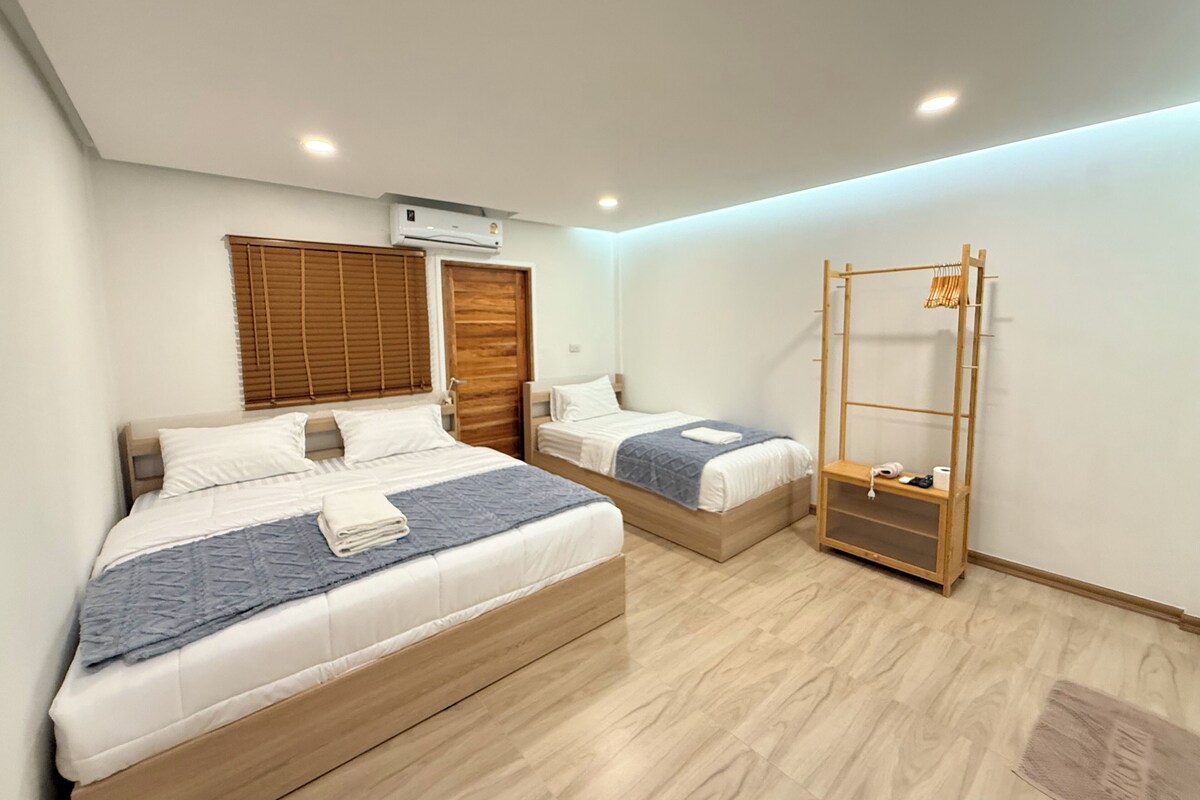 A bedroom with two beds, a wooden wardrobe, a wooden drying rack, and a ceiling-mounted air conditioner.