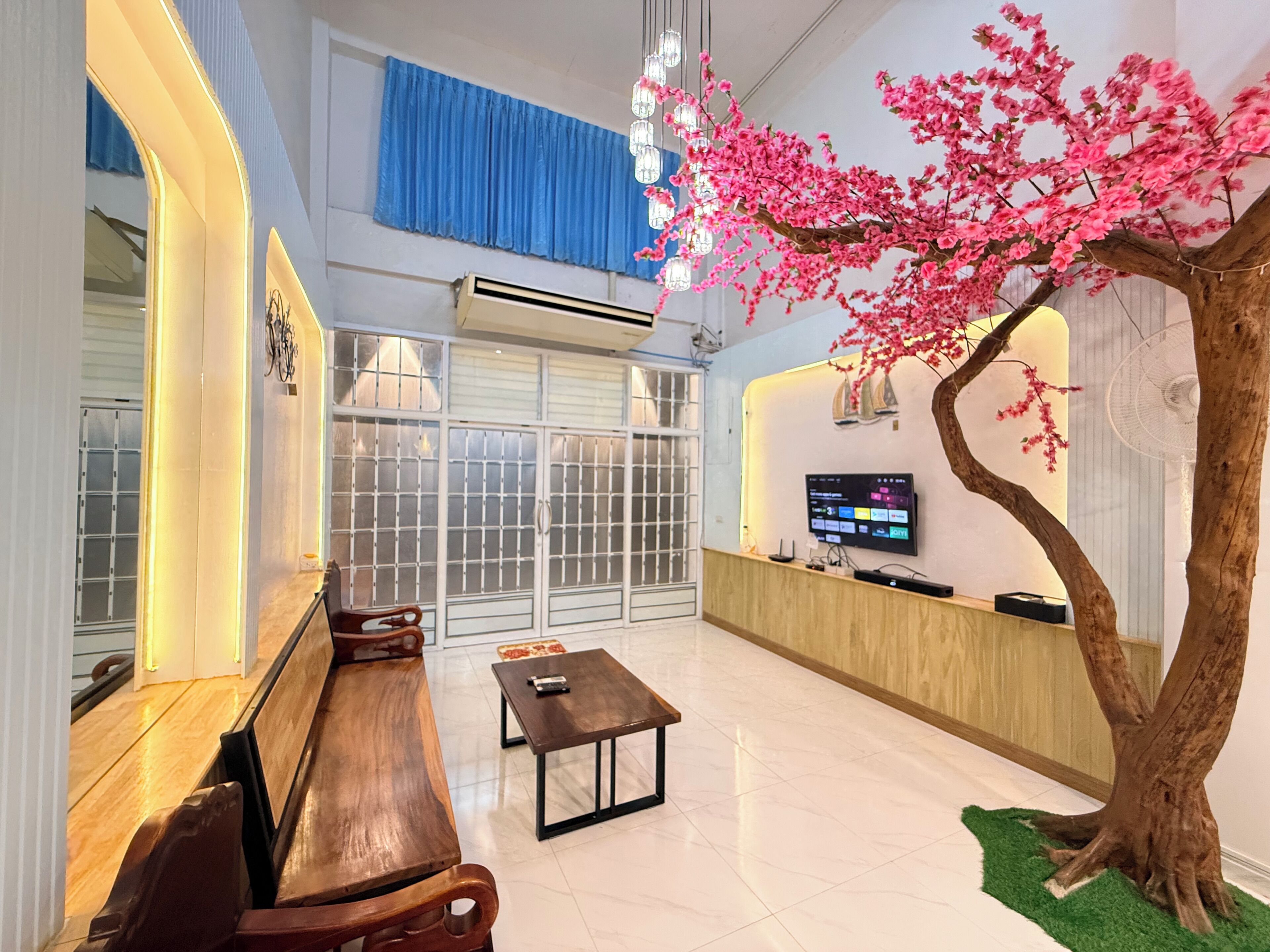 A reception area with a wooden bench, a small table, a TV mounted on the wall, and a decorative tree with pink flowers.