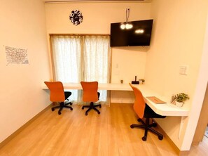 A room with a wooden floor, a white desk, three orange chairs, a black TV on the wall, and a window with curtains. - Upper Hotel Ryogoku (Tokyo)