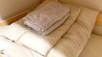 A bed with a folded towel and pillows, wooden headboard, and light-colored walls.