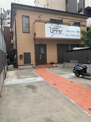 A hotel named 'Upper Hotel' with a signboard, a scooter parked in front, and a red pathway leading to the entrance. - Upper Hotel Ryogoku (Tokyo)