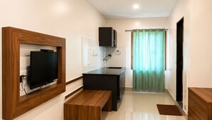 Une chambre d’hôtel compacte équipée d’une télévision, d’une kitchenette, d’un banc en bois et d’un lit.