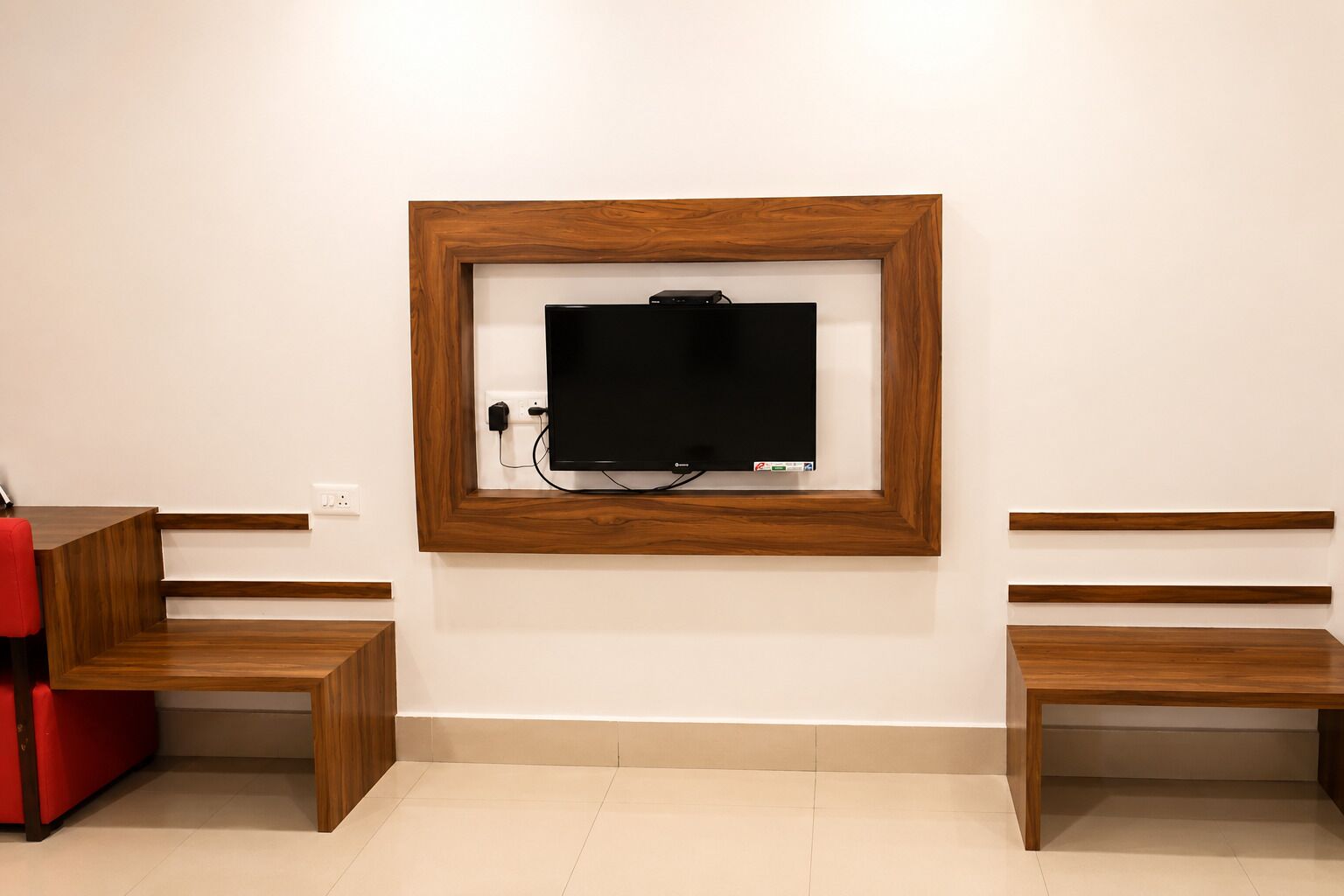 Une pièce avec un téléviseur fixé au mur, des bancs en bois et un fauteuil rouge.