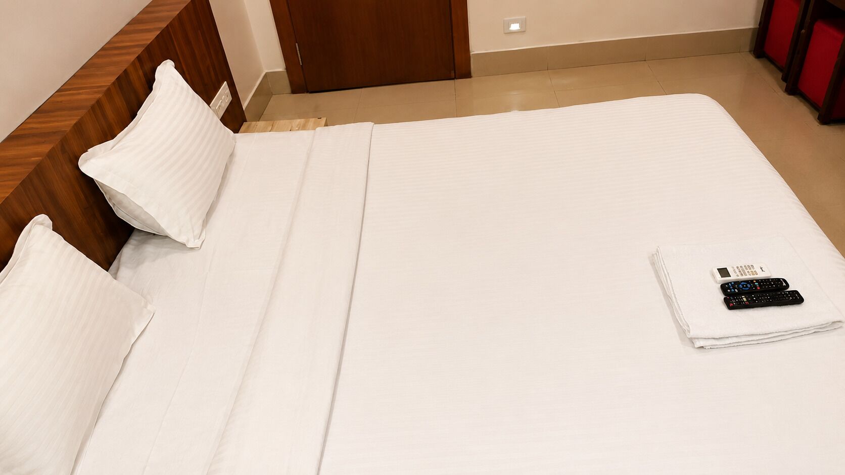 Una cama bien hecha con almohadas y un control remoto sobre el edredón.