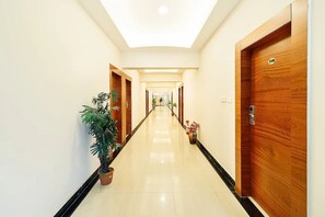 A hotel corridor with wooden doors, potted plants, and a tiled floor. - SRS Jade Empire (Anekal)