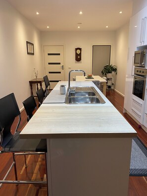 A modern kitchen with a central island, stainless steel appliances, and a dining area with chairs. - Eastern Suburbs Gem (Forest Hill)