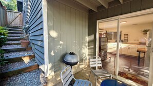 Eine Terrasse mit Stufen zu einer Tür, einem Grill und zwei Metallstühlen.